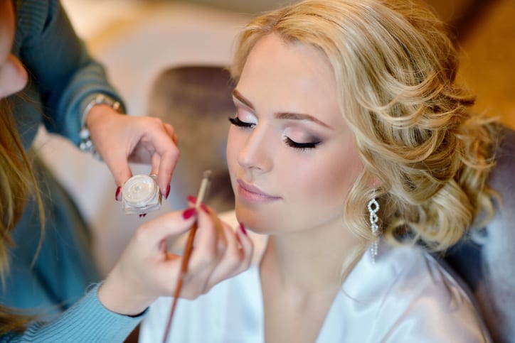 Wedding makeup artist making a make up for bride. Beautiful sexy model girl indoors. Beauty woman with curly hair. Female portrait. Bridal morning of a cute lady. Close-up hands near face